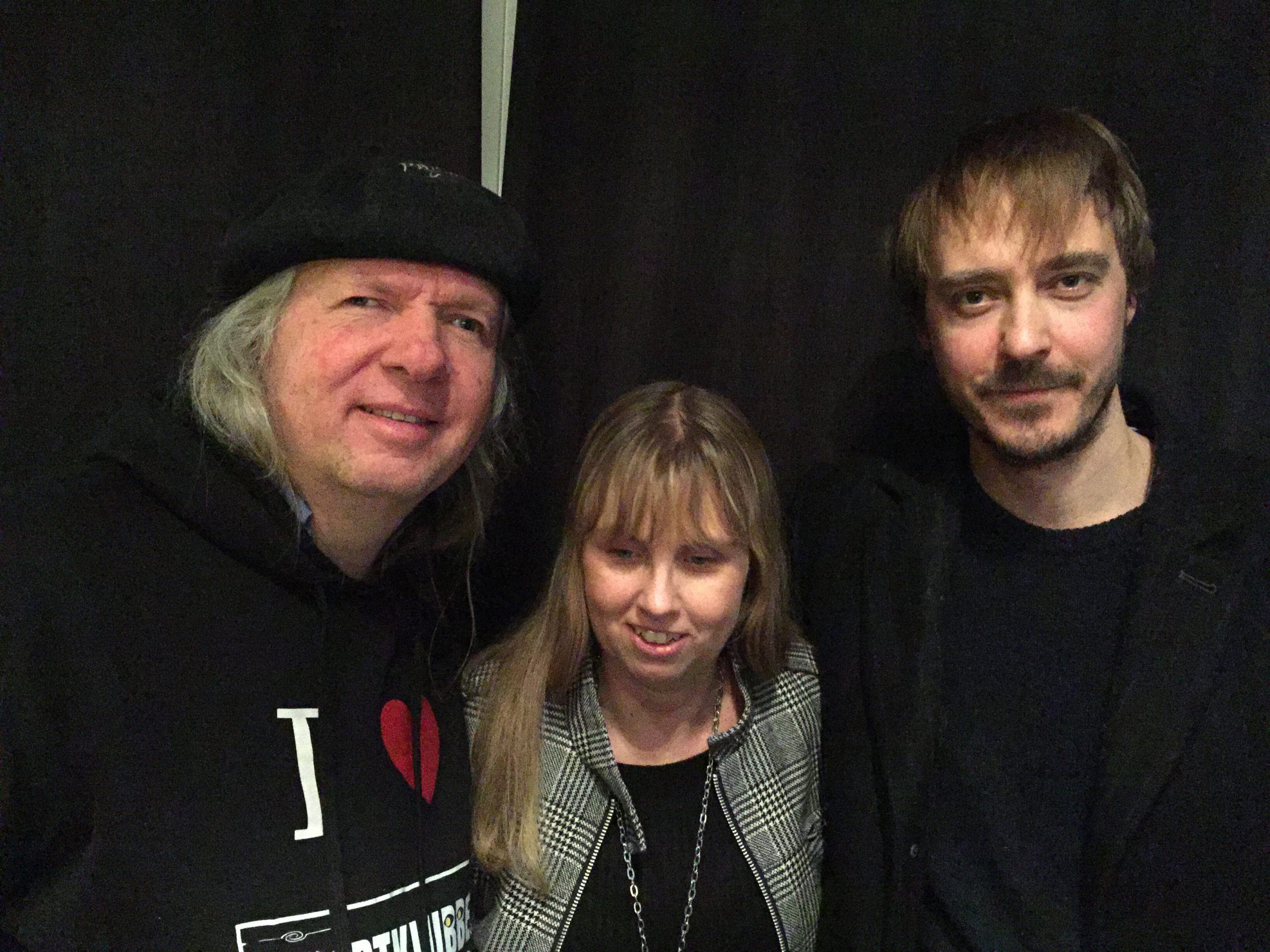 Ulf, Anna och Jonas i studion med svarta drapperier som bakgrund. Ulf har en svart huvudbonad, grått hår och en svart munktröja med texten: I love Svartklubben. Anna har långt blont hår med lugg framtill, en svart topp under en grårutig kavaj. Jonas har brunt kort hår med lugg framtill, mustasche, skägg och en svart tröja.