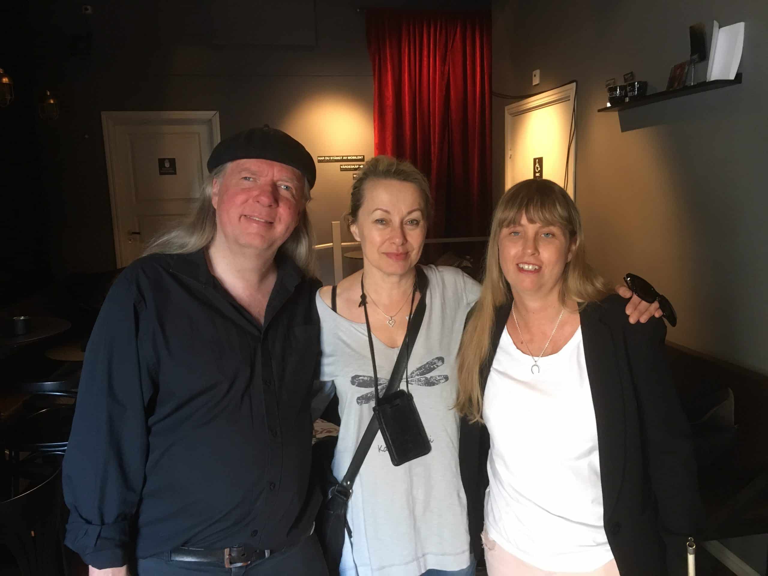 Ulf, Louise och Anna, gruppfoto i studion med röda gardiner som bakgrund. Ulf har en svart basker, långt grått hår, svart skjorta och svarta byxor. Louise har långt blont uppsatt hår, en ljus tröja. Runt överkroppen hänger en svart axelremsväska och en halsrem med en mindre svart väska framtill. Anna har långt blont hår med lugg framtill. Hon har på sig en svart långärmad tröja och vit undertröja.