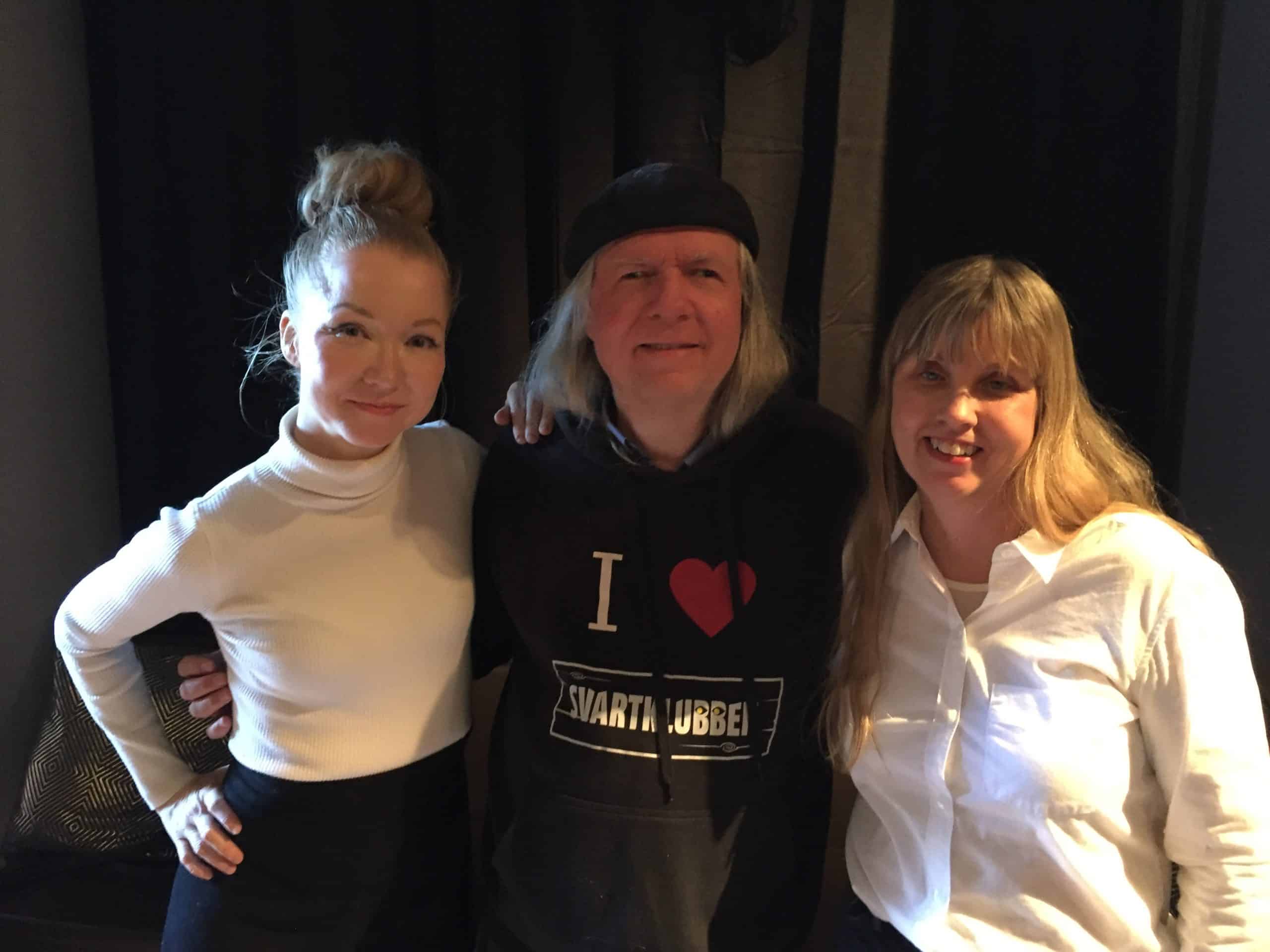 Gruppfoto, Angela, Ulf och Anna i studion. Angela har mörkblont långt hår uppsatt i en toffs ovanpå huvudet och har på sig en vit polotröja och svart kjol. Ulf har på sig en svart basker samt en huvtröja med texten I love Svartklubben. Anna har långt blont hår och lugg framtill. Hon har på sig en vit långärmad skjorta. Bakgrunden är mörk och diffus.