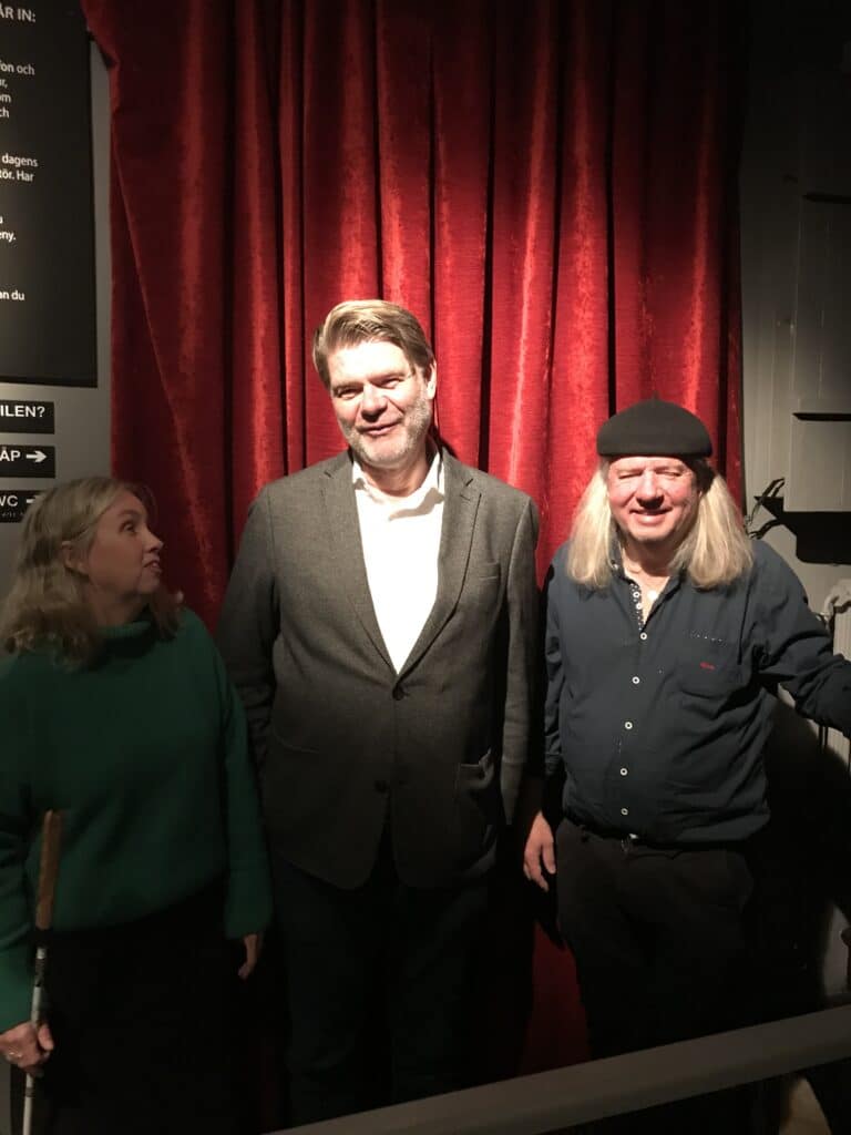 Anna, Björn och Ulf i studion framför rött draperi. Anna håller i en vitkäpp, är vänd mot Björn, klädd i en grön polotröja och har axellångt blont hår. Björn har kort brunt hår, kort skägg, grå kavaj med vit skjorta. Ulf har svart basker, långt grått hår och en svart skjorta på sig. Björn och Ulf tittar rakt mot kameran och ler.